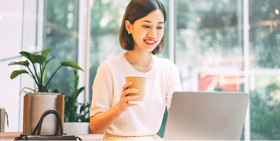 カフェでパソコンを操作しながらコーヒーを持つ女性