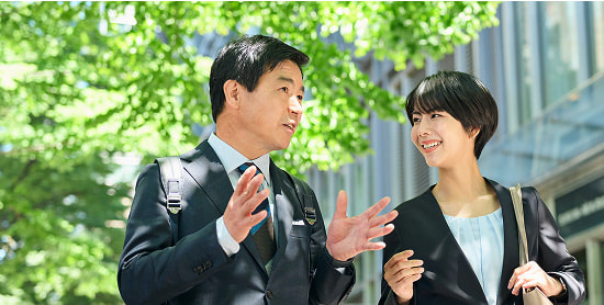 屋外で会話をしながら歩くスーツ姿の男女